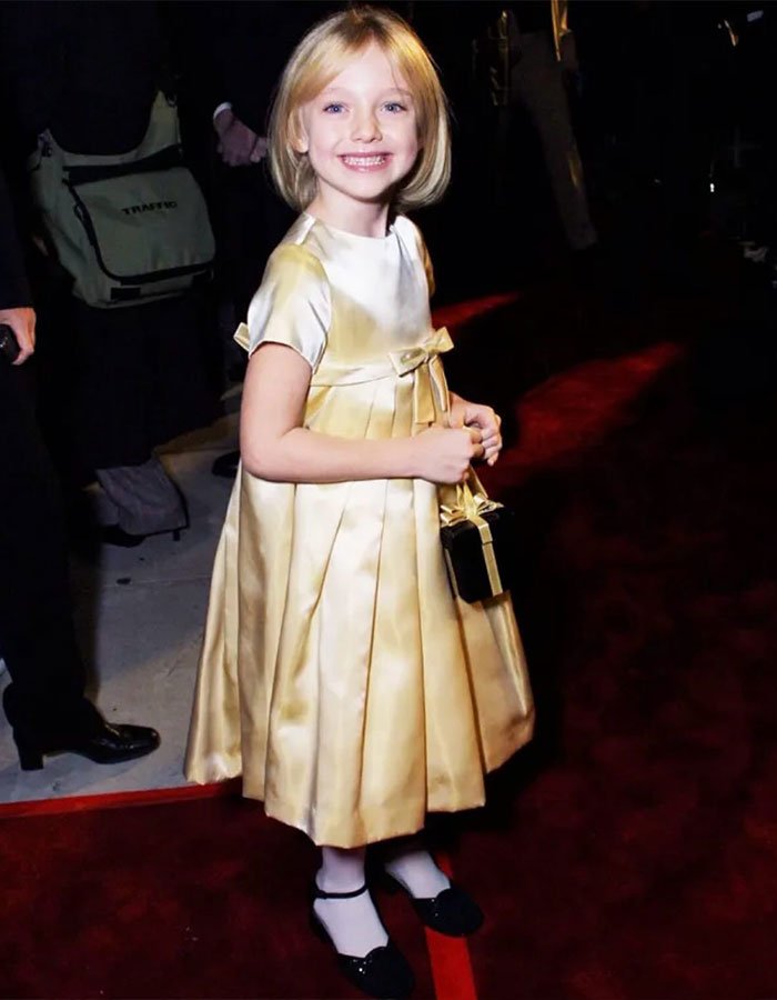 Young Dakota Fanning smiling on the red carpet in a gold dress, highlighting confusion over Fanning’s real names in media.