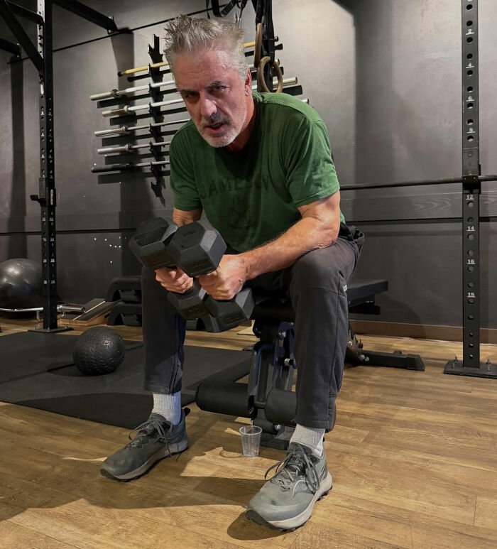 Chris Noth lifting dumbbells in a gym, breaking silence after savage off the cuff dig sparking fan backlash.