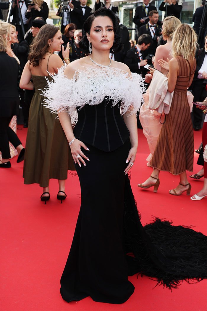 Woman on a red carpet in a black gown with white feather details, accused of plagiarizing Arab influencer’s look at the Golden Globes.