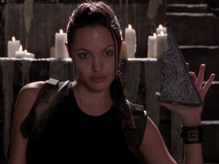 Female action hero holding an ancient artifact with candles in the background, highlighting a Lara Croft transformation.