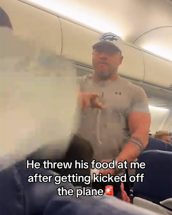 Muscular bodybuilder in gray shirt and cap confronting elderly passenger on airplane showing fury before removal.