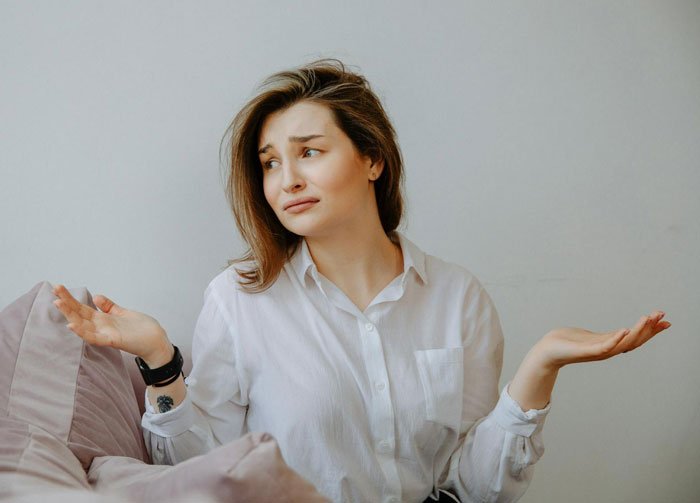 Young woman in white shirt shrugging with a puzzled expression, illustrating MIL thinks she’s won against DIL conflict.