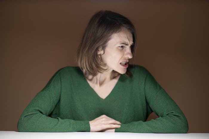 Woman in green sweater showing frustration and anger, representing MIL thinks she’s won against DIL tension and rearranging furniture.