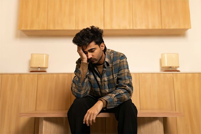 Man in a plaid shirt sitting on a bench looking frustrated, illustrating workplace bully revenge theatrics concept.