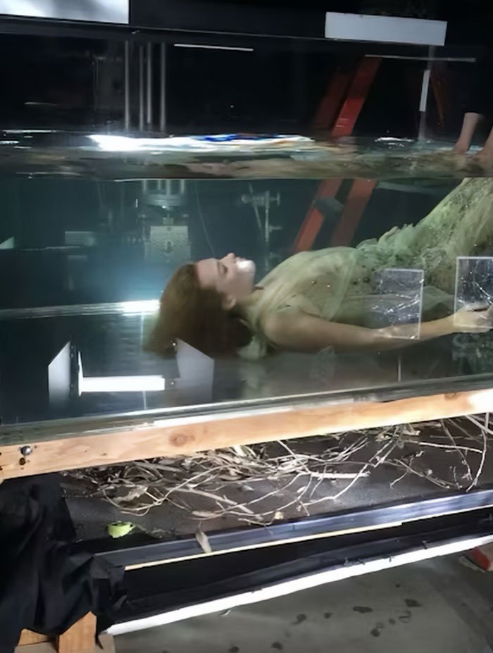 Margot Robbie lying underwater in a dress during a controversial underwater cover shoot setup with visible studio equipment.