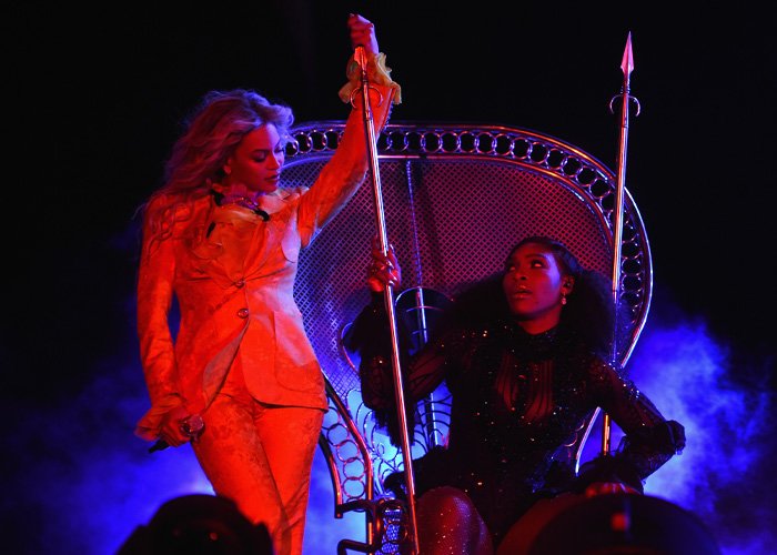 Serena Williams performing a viral jaw-dropping move with knees kneeling on stage in dramatic lighting and costume.