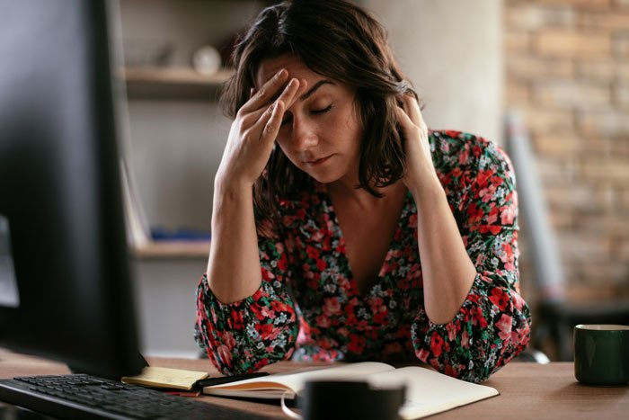 Stressed mom of six sitting at desk with head in hand, feeling overwhelmed while babysitting brother’s son.