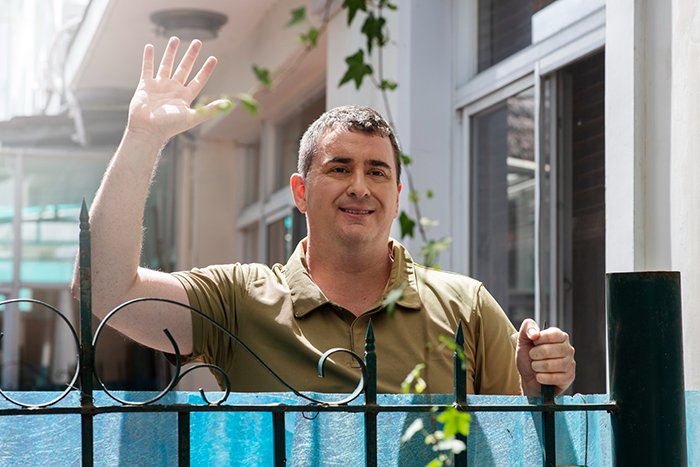 Man waving behind a metal fence outdoors, symbolizing a guy’s heroic actions and his personal journey of self-discovery.
