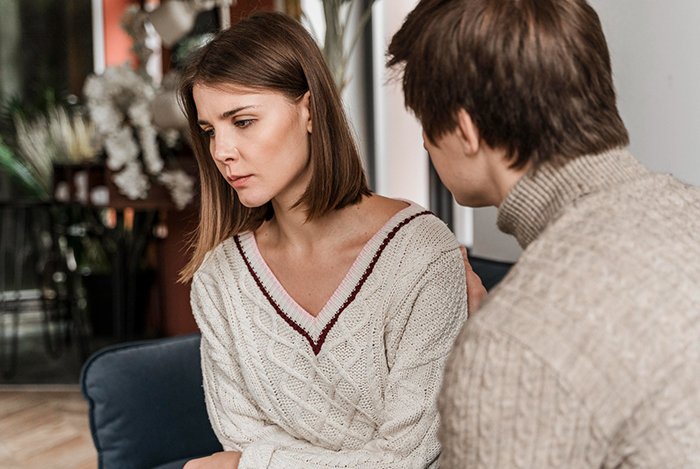 Young man showing concern to a sad woman, illustrating guy’s heroic actions and relationship struggles in a casual indoor setting.