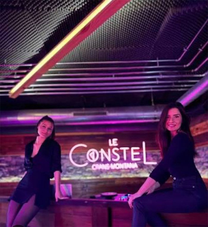 Two women posing inside a dimly lit bar with neon lighting, related to waitress who escaped Swiss bar fire story.