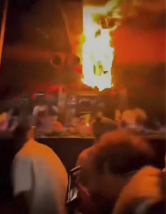 Blurry scene of a Swiss bar fire with patrons in the foreground and bright flames engulfing part of the interior.