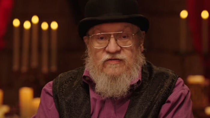 George RR Martin wearing a black hat and glasses, speaking about the shocking intro scene in A Knight of the Seven Kingdoms.
