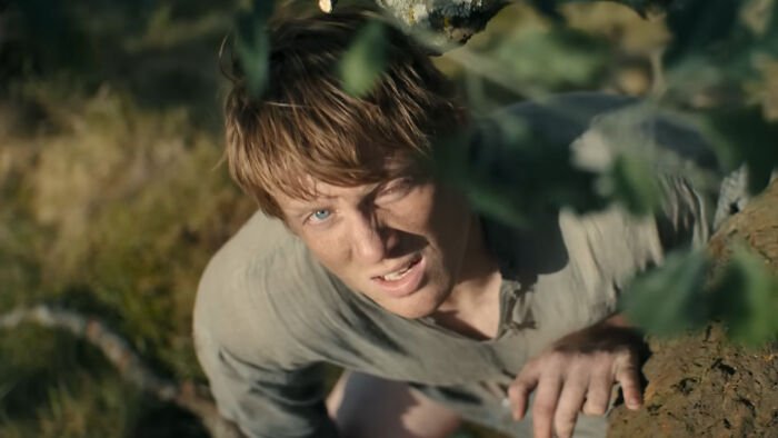 Young man climbing a tree in a forest scene from A Knight of the Seven Kingdoms, related to George RR Martin’s work.