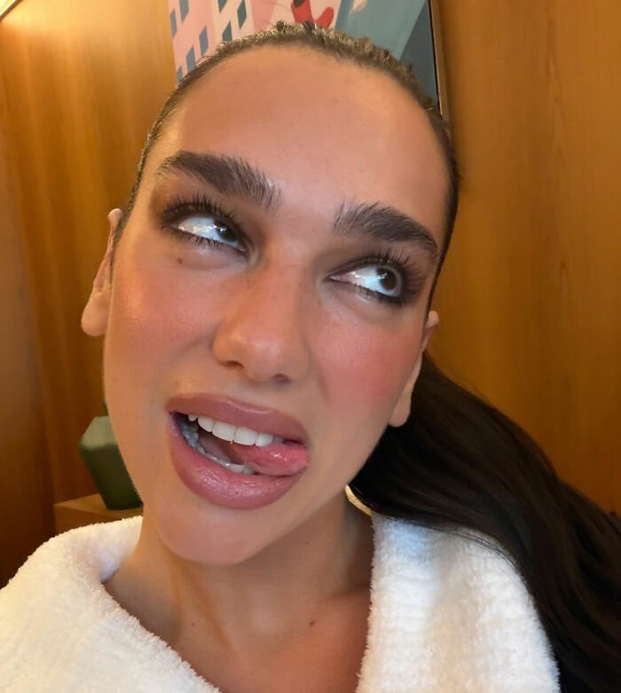 Dua Lipa making a playful face indoors, reacting with surprise to a fan’s filter during a selfie moment.