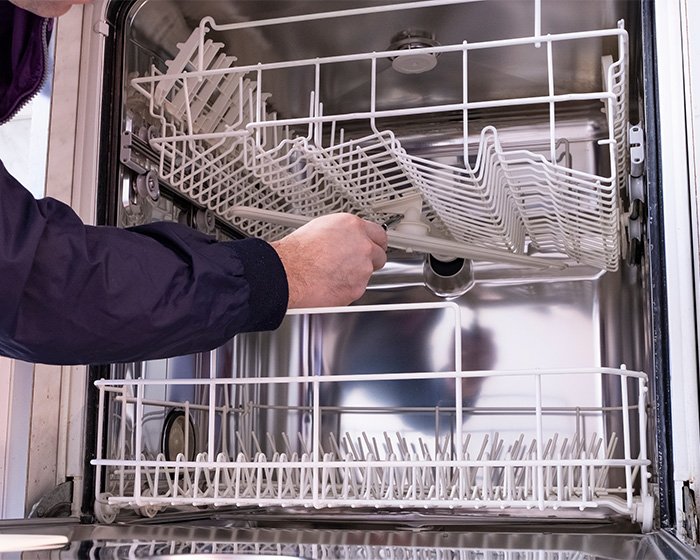 Hand opening empty dishwasher rack inside stainless steel dishwasher, focusing on dishwasher appliance and racks.