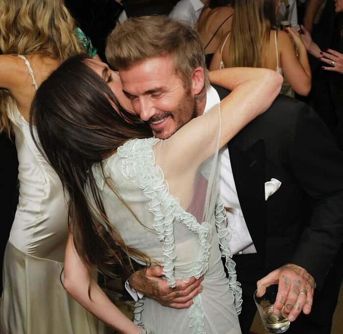 Victoria Beckham dancing at an event, embracing a man in a suit while surrounded by people in formal attire.