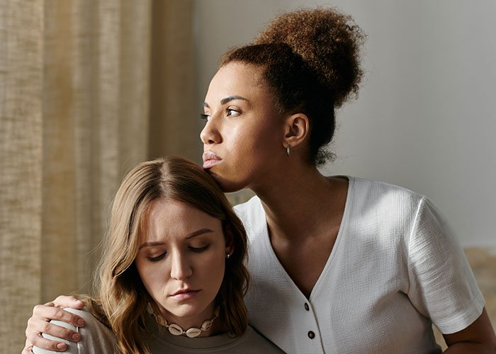 Two women showing emotions, one comforting the other after fabricating evidence of cheating to convince friend to dump boyfriend.