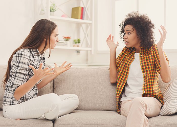 Two women on a couch having a heated argument, illustrating woman fabricates evidence of cheating and plan backfires.