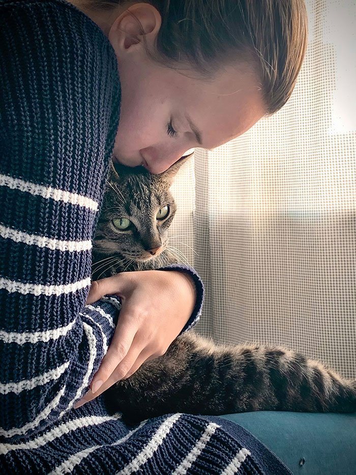 Woman in a striped sweater hugging her cat closely indoors, illustrating a cat disappearing for days and neighbor adopting him.