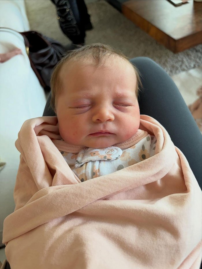 Newborn baby peacefully sleeping wrapped in a pink blanket, related to Meghan Trainor's secret surrogate baby news.