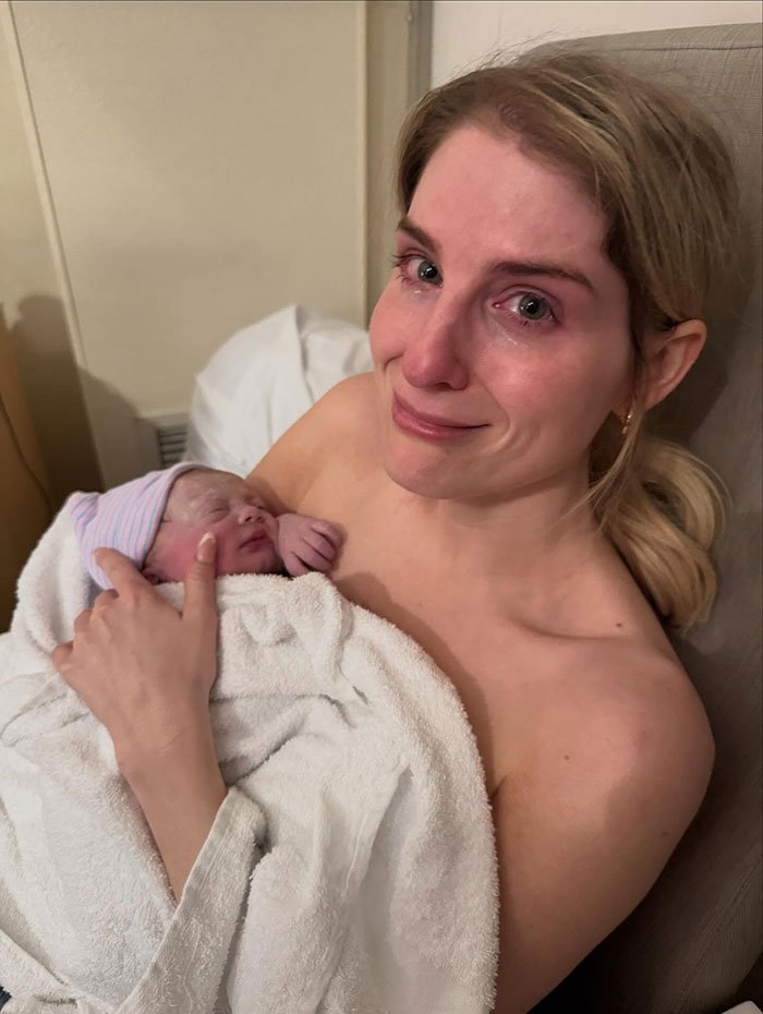Woman holding newborn baby wrapped in white towel, emotional moment captured with secret surrogate baby reveal.