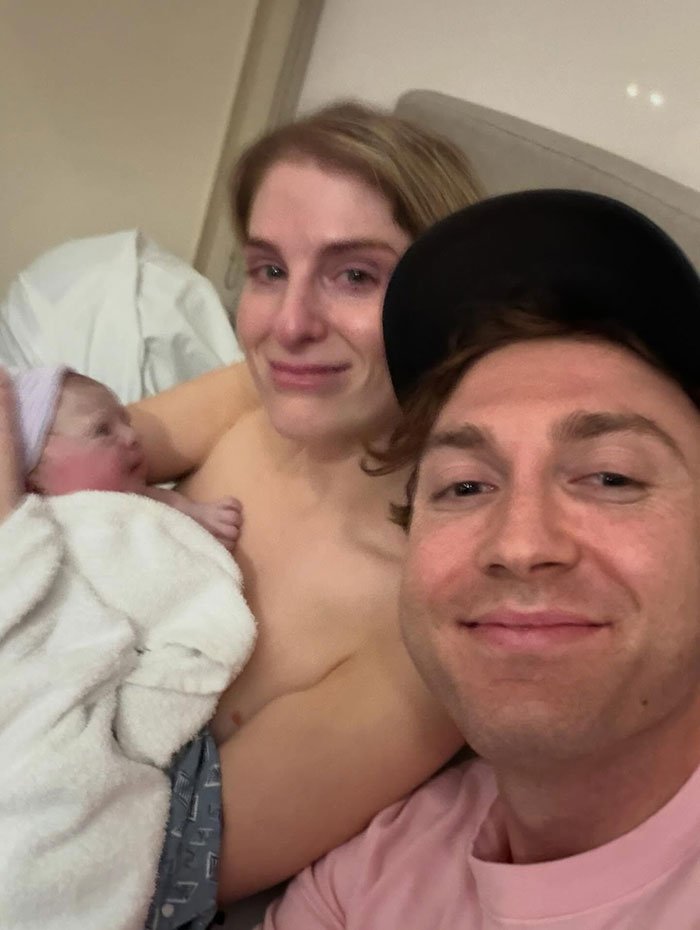New parents smiling with their newborn wrapped in a blanket in a hospital room, highlighting surrogate baby news.