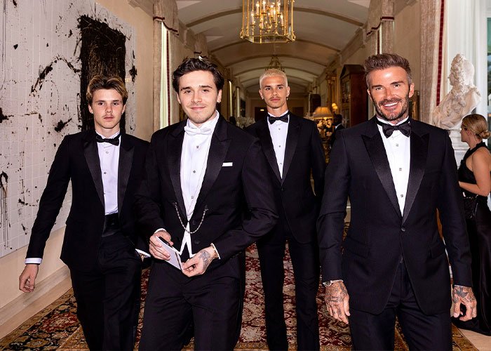 Four men in black tuxedos walking down a hallway at a wedding event, related to Victoria Beckham’s dance details.