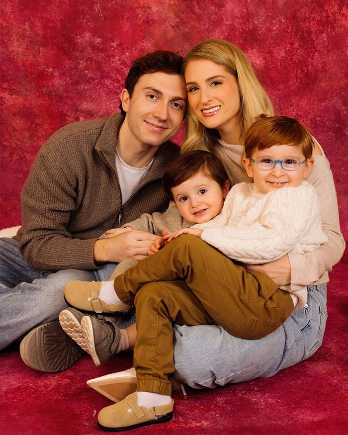 Meghan Trainor with family sitting closely together against a red backdrop, highlighting surrogate baby and backlash discussion.