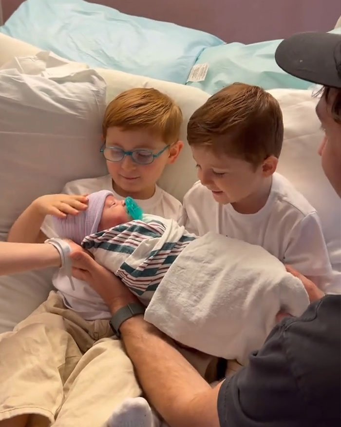 Two young boys and a man holding a newborn baby, highlighting Meghan Trainor surrogate baby family moment.