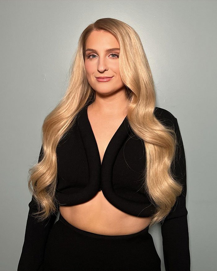 Meghan Trainor posing with long blonde hair and black outfit, addressing why she used a surrogate for her baby.