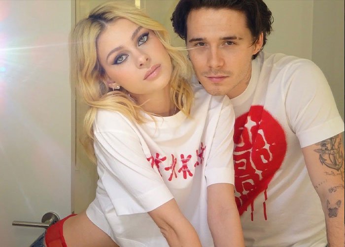 Blonde woman and man wearing white shirts, posing closely indoors with soft natural light in casual setting.