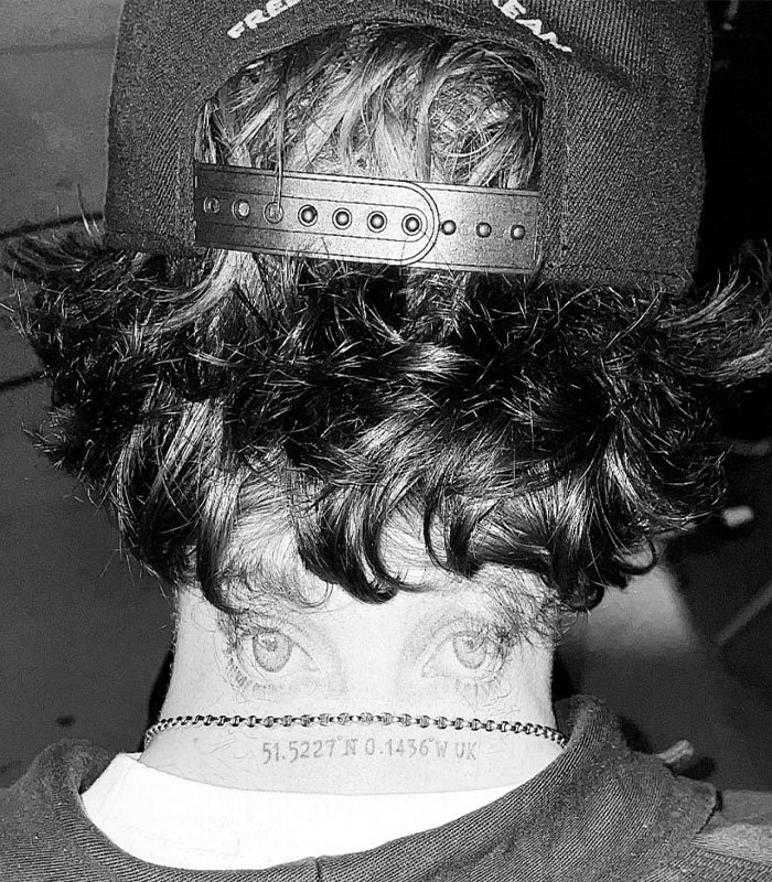Black and white image showing the back of a person's head with a cap and a tattoo of eyes and coordinates on the neck, sister of Nicola Peltz's ex.