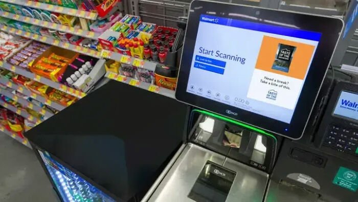 Self-checkout station at Walmart store displaying start scanning screen with various snacks nearby and theft detection.