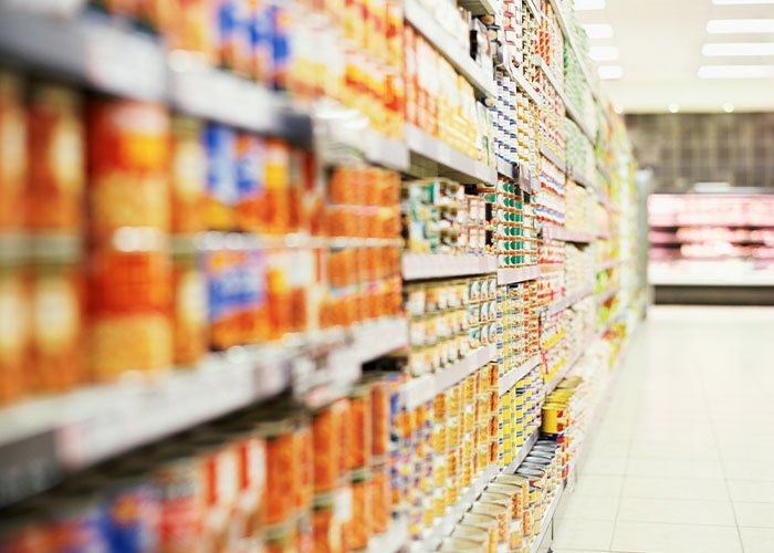 A grocery store aisle filled with stacked canned goods under bright fluorescent lighting.