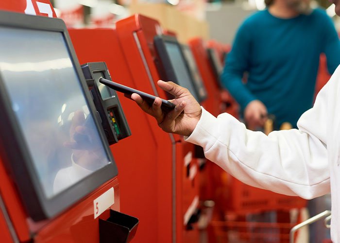 Person using a smartphone to scan payment at a Walmart self-checkout kiosk in a retail store setting.