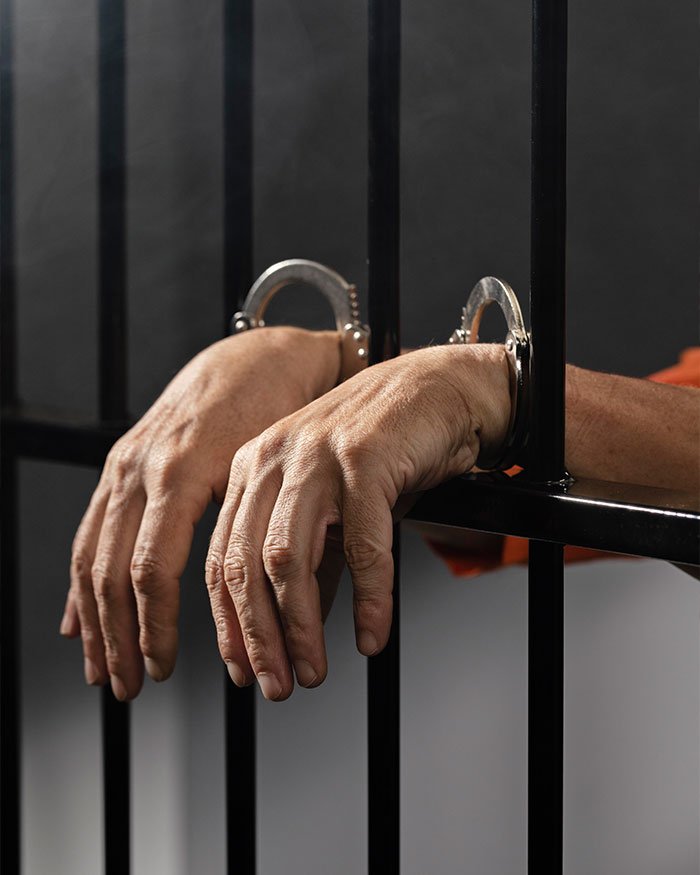 Hands in handcuffs behind jail bars symbolizing assistant principal accused in Walmart theft scheme using stacking method.