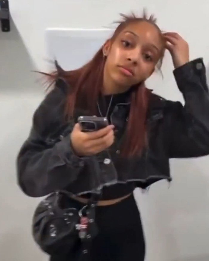 Teen client in a salon holding a phone with red hair after incident involving Maryland hairstylist dragging her by hair