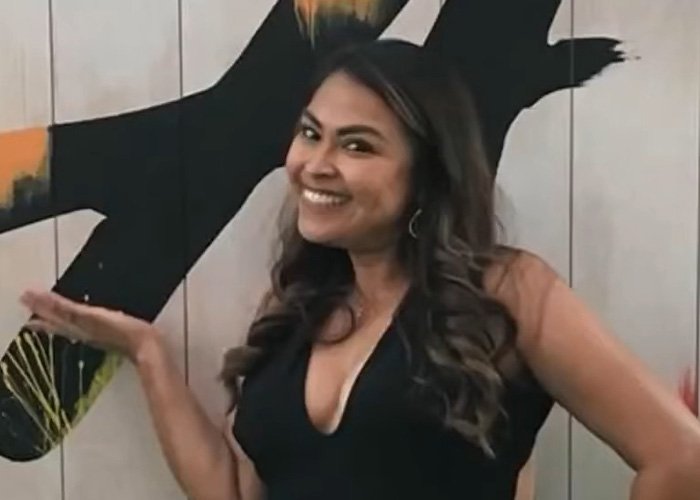 Smiling woman with long hair posing indoors with an abstract black and orange wall art behind her, representing teacher’s life story.