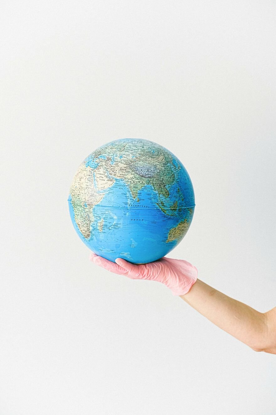 Hand wearing a pink glove holding a blue globe representing Earth, symbolizing the concept of Earth cost evaluation.
