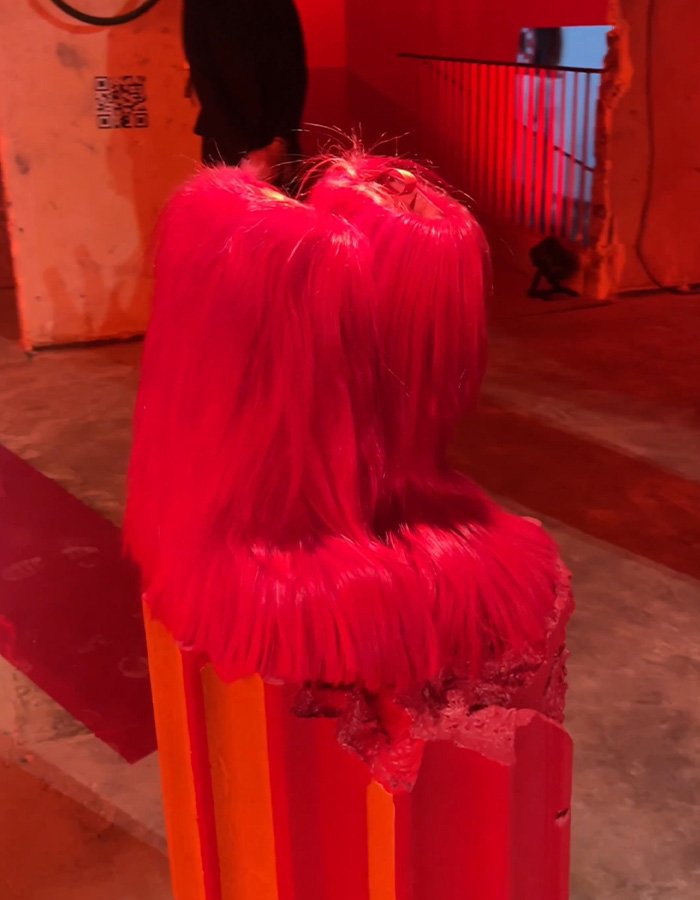 Three vibrant pink furry boots displayed on an orange and red platform at a fashion event for Christian Louboutin collection.