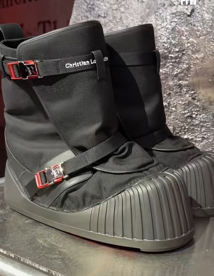 Black Christian Louboutin sneakers with red buckles and textured soles displayed on a metallic surface.