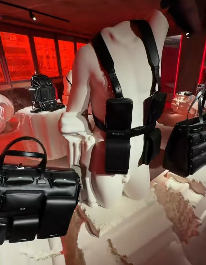 Christian Louboutin black leather bag collection displayed on white mannequins in a red-lit showroom setting.