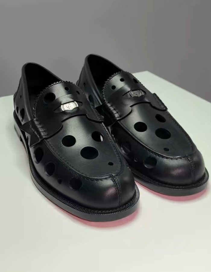 Black leather shoes with perforated holes and decorative metal detail showcased on a white surface in studio lighting.