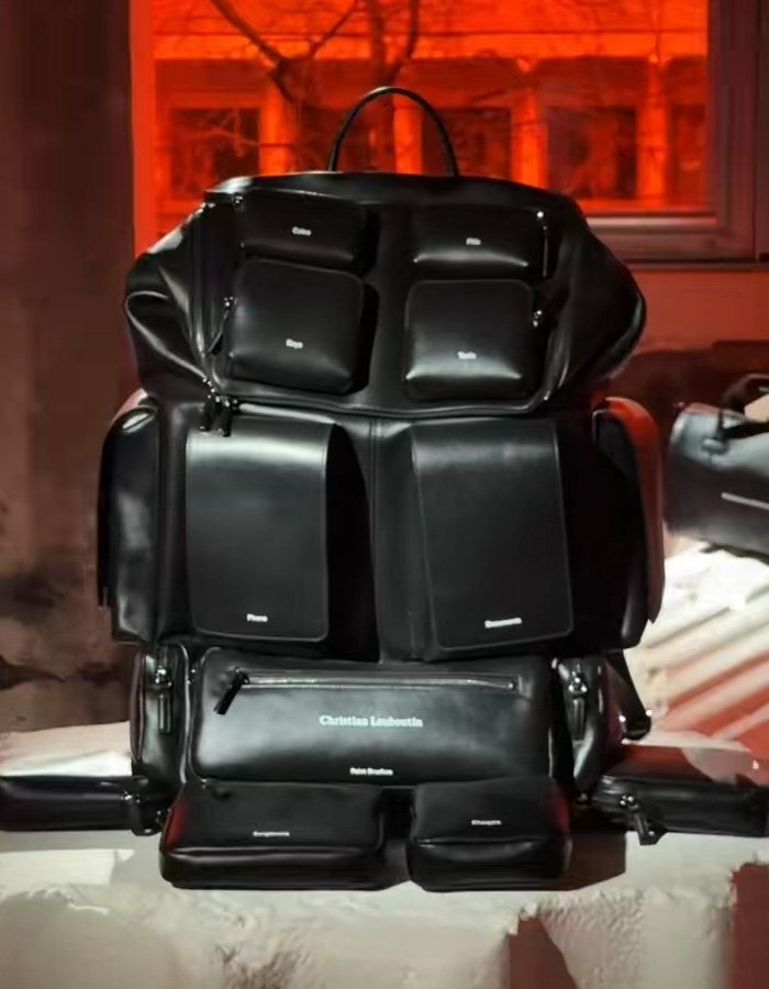Black Christian Louboutin bag with multiple compartments displayed indoors under orange lighting.