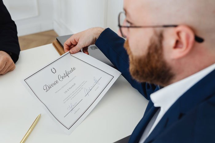 Man in glasses and suit holding a divorce certificate during a discussion, illustrating complex family dynamics with multiple parents.