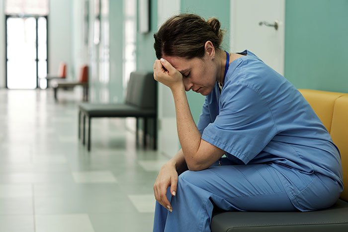 Woman in scrubs sitting in a hospital hallway looking stressed, reflecting career lies and wild stories she made up