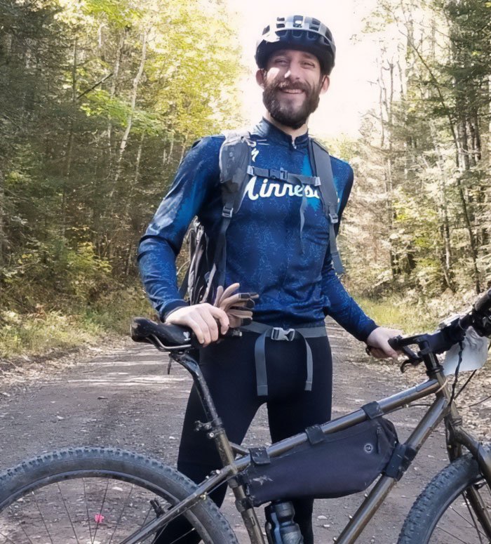 Man with a bike smiling outdoors in forest, representing Alex Pretti’s parents learning his fate from a reporter.