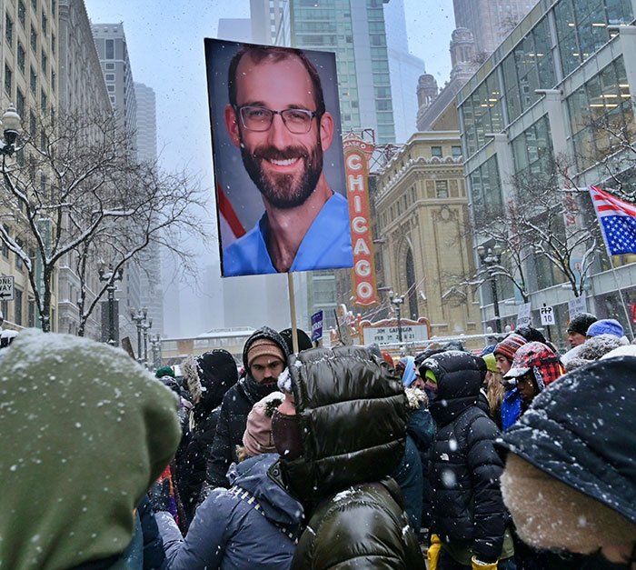Crowd in snowy Chicago holding a large portrait, reflecting heated debate and protests related to ICE and Michael Che on SNL.
