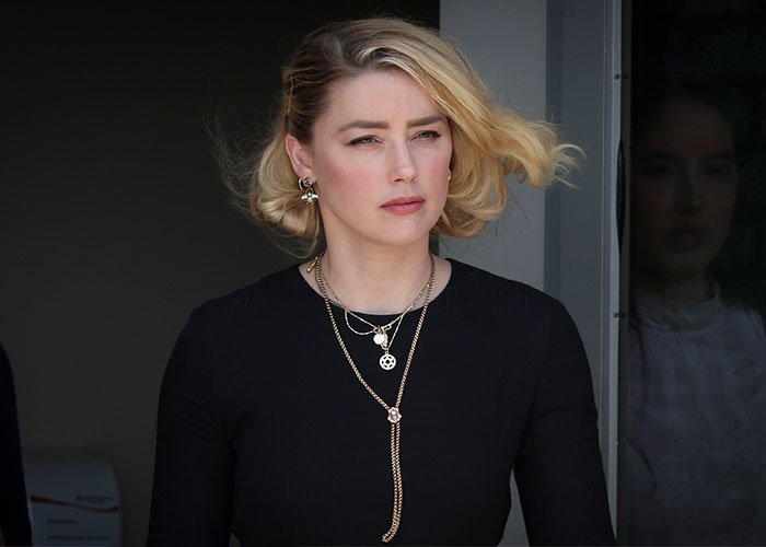 Amber Heard in a black top and layered necklaces appearing serious for a documentary on defamation suits and the Depp trial.