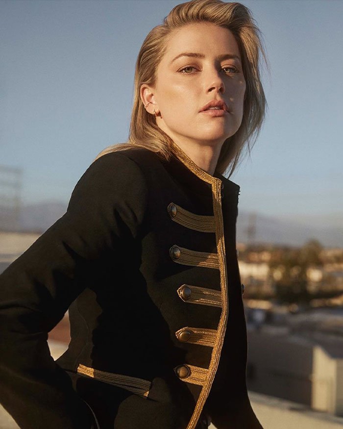 Amber Heard posing outdoors in a black jacket, featured in a documentary revisiting defamation suits and the Depp trial.